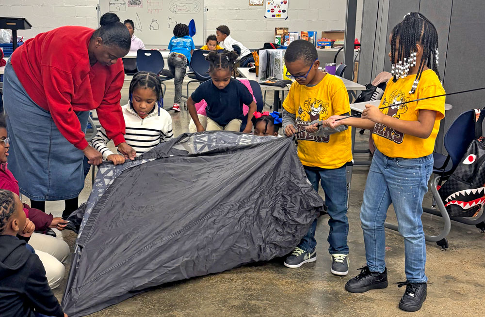 A teacher and children assemble a camping tent